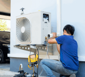 Technicien en climatisation répare ou installe une unité extérieure de climatiseur avec des outils, y compris un manomètre jaune.
